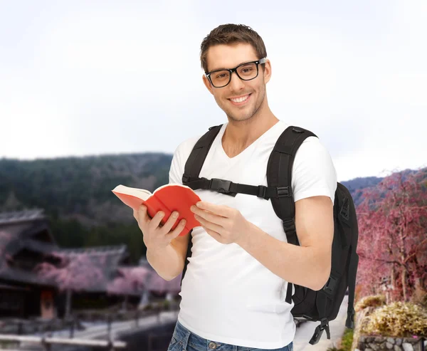 Glücklicher junger Mann mit Rucksack und Buch unterwegs — Stockfoto