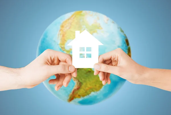 Пара рук держа зеленый дом над земным шаром — стоковое фото