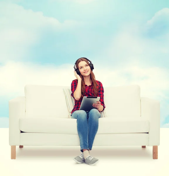 Girl sitting on sofa with headphones and tablet pc — Stock Photo, Image