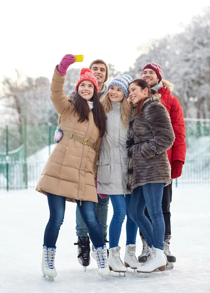 Happy friends with smartphone on ice skating rink — Stock Photo, Image