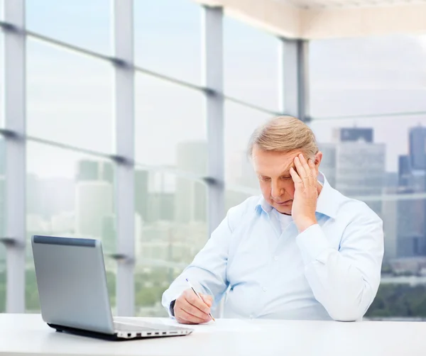 Senior man met laptop en pen schrijven op kantoor — Stockfoto