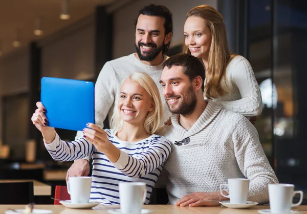 Счастливые друзья с планшетным компьютером, делающие селфи в кафе — стоковое фото