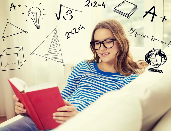 Улыбающаяся девочка-подросток читает книгу на диване — стоковое фото