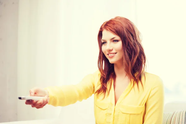 Smiling young woman with tv remote control at home — Stock Photo, Image