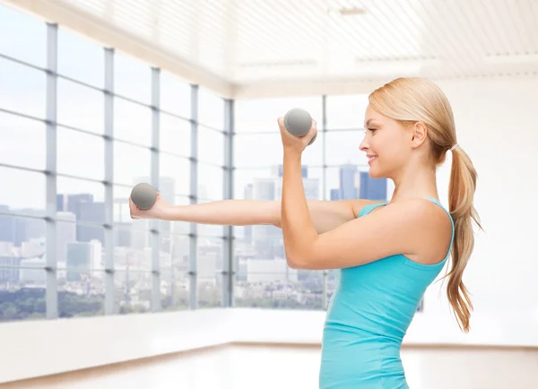 Donna sorridente con manubri che flettono bicipiti in palestra — Foto Stock