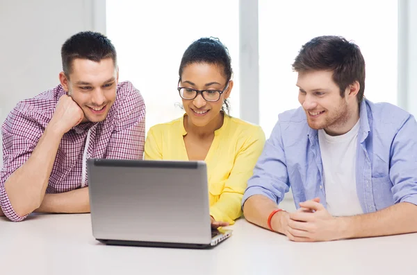 Трое улыбающихся коллег с ноутбуком в офисе — стоковое фото