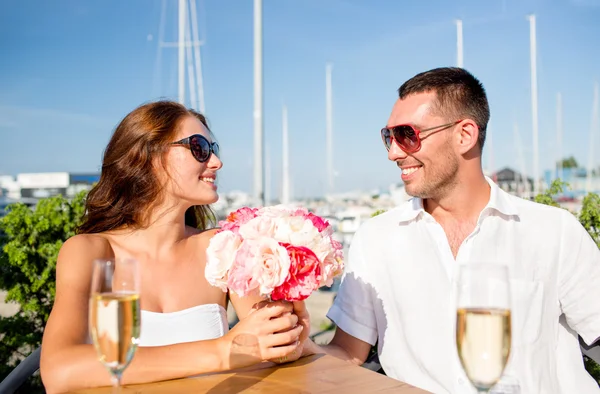 Smiling couple with bunch and champagne at cafe — Stock Photo, Image