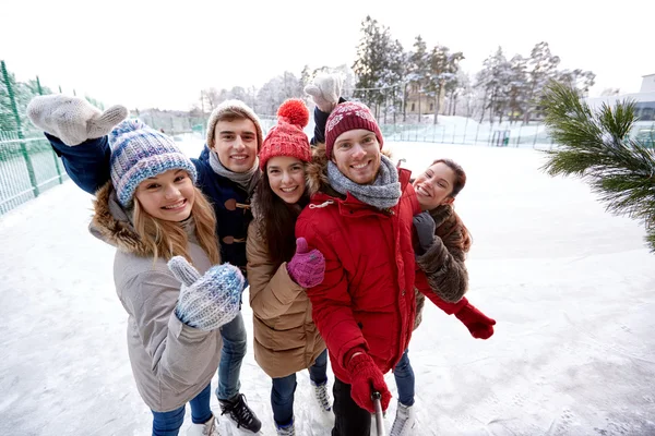 Amigos felizes com smartphone na pista de patinação no gelo — Fotografia de Stock