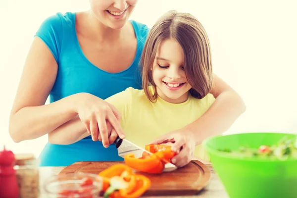 Lächelndes kleines Mädchen mit Mutter, die Paprika hackt — Stockfoto