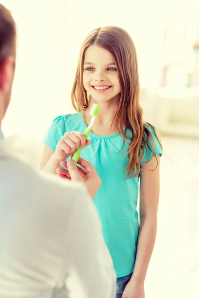 Αρσενικό γιατρός δίνοντας οδοντόβουρτσα με χαμογελαστό κορίτσι — Φωτογραφία Αρχείου