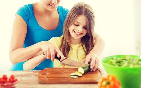 Niña sonriente con madre cortando pepino — Foto de Stock