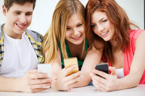 Drie lachende studenten met smartphone op school — Stockfoto