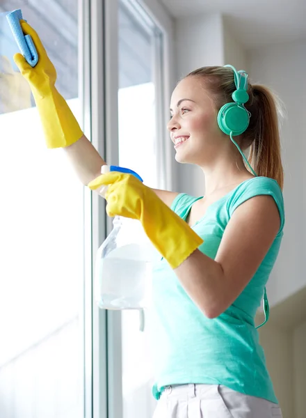 Wanita bahagia dengan headphone membersihkan jendela — Stok Foto