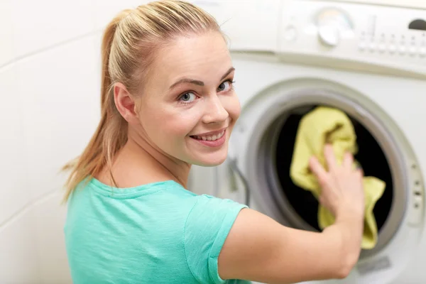 Mulher feliz colocando roupa na máquina de lavar em casa — Fotografia de Stock