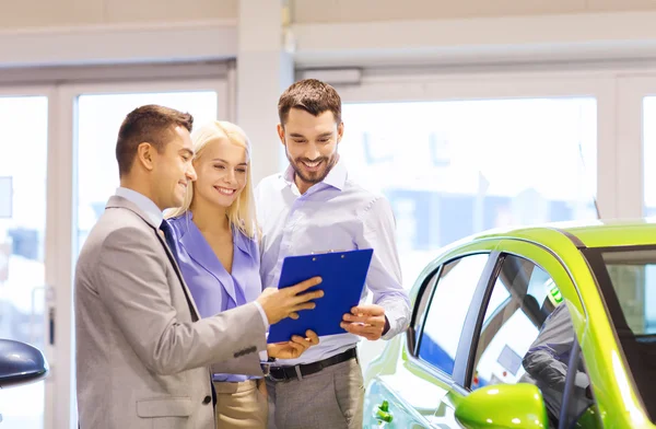 Glückliches Paar mit Autohändler in Auto-Show oder Salon — Stockfoto