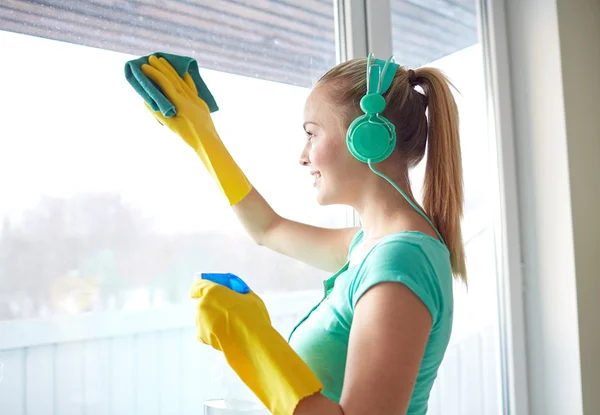 Happy woman with headphones cleaning window — Stock Photo, Image