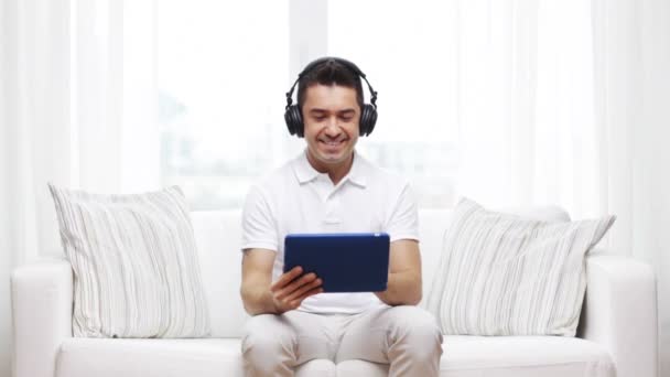 Uomo sorridente con tablet pc e cuffie a casa — Video Stock