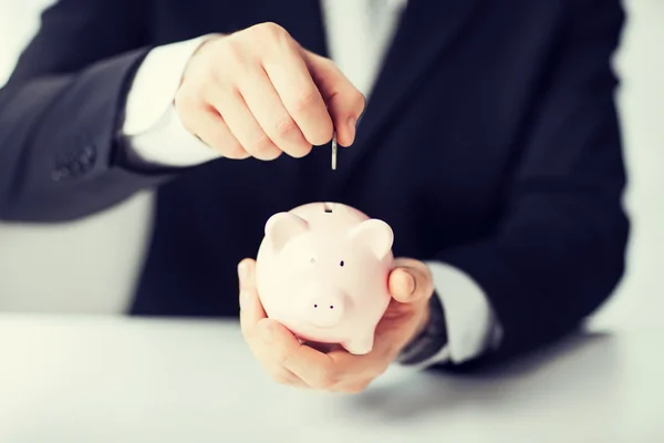 Man putting coin into small piggy bank — Stock Photo, Image