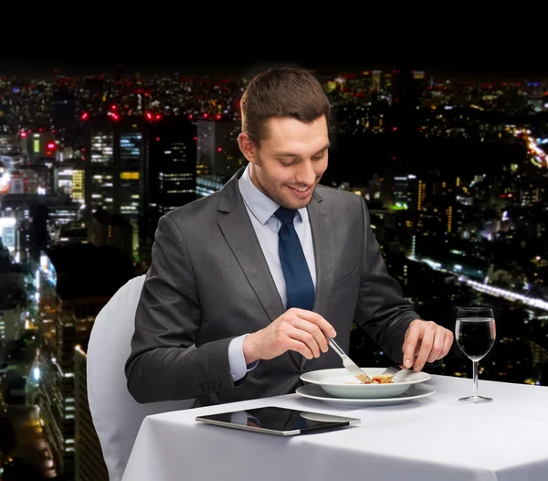 Homem sorridente com tablet pc comendo prato principal — Fotografia de Stock
