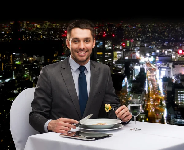 Homem sorridente com tablet pc comendo prato principal — Fotografia de Stock