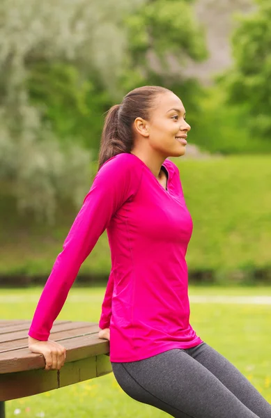 Sonriente mujer haciendo flexiones en el banco al aire libre — Foto de Stock