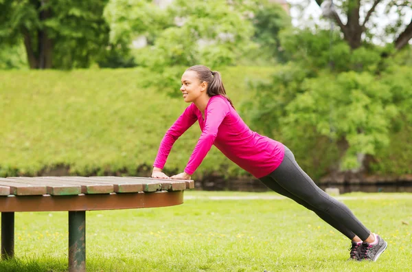 Femme souriante faisant push-ups sur le banc à l'extérieur — Photo