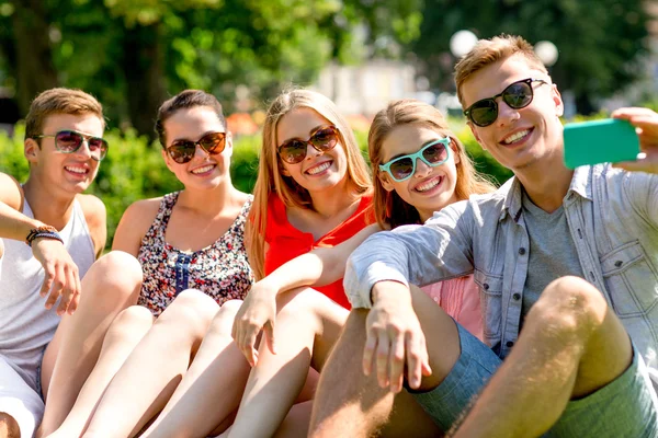 Amigos sonrientes con teléfono inteligente sentado en la hierba — Foto de Stock