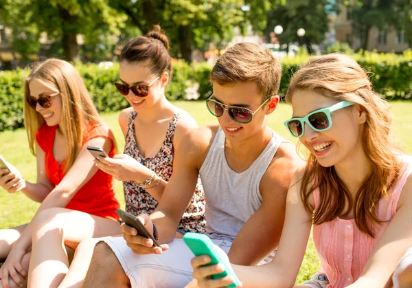 Amigos sonrientes con teléfonos inteligentes sentados en la hierba — Foto de Stock