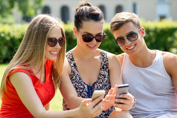 Lächelnde Freunde mit Smartphones im Park lizenzfreie Stockbilder