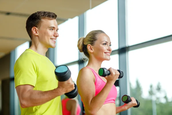 Uomo e donna sorridente con manubri in palestra — Foto Stock