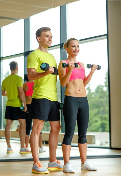 Sonriente hombre y mujer con mancuernas en el gimnasio — Foto de Stock