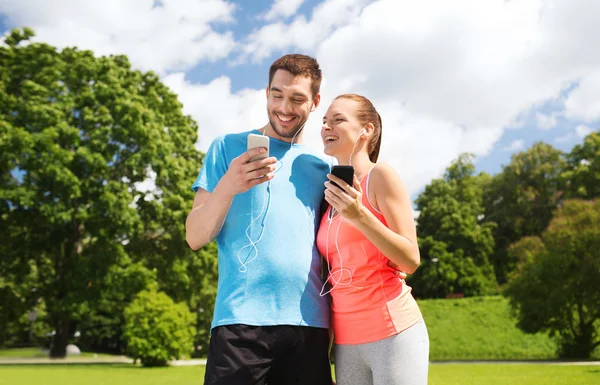 Due persone sorridenti con smartphone all'aperto — Foto Stock