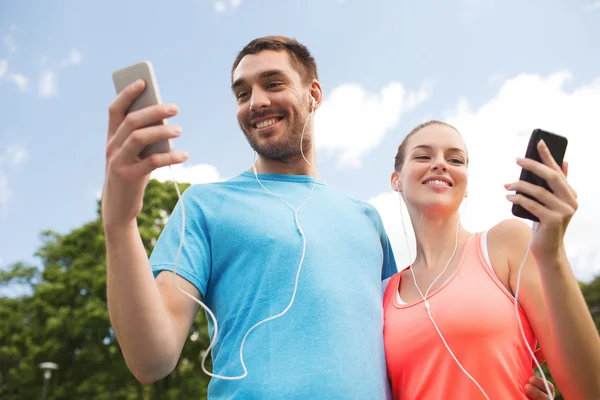Два улыбающихся человека со смартфонами на улице — стоковое фото