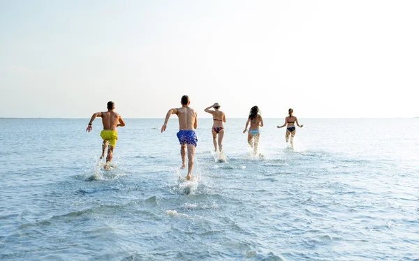 Amigos sonrientes corriendo en la playa desde atrás — Foto de Stock