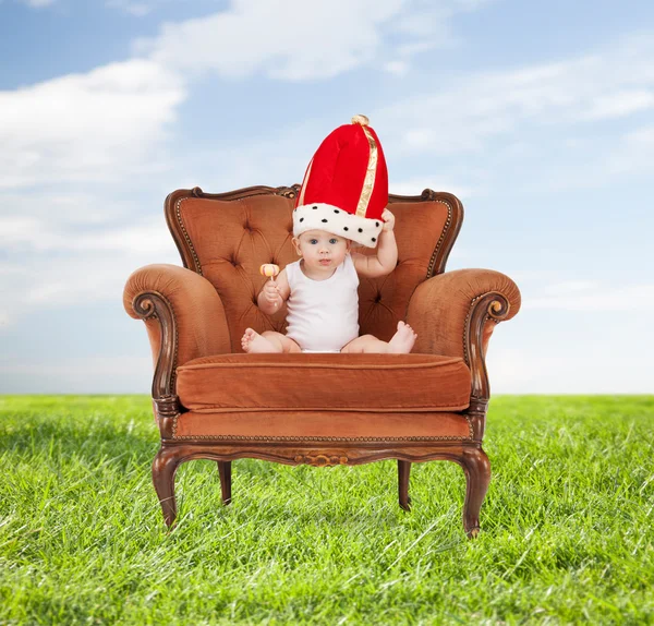 Dziecko w królewskim kapelusz z lizak siedzi na krześle — Zdjęcie stockowe