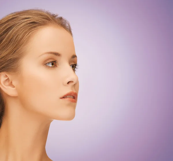 Mooie jonge vrouw gezicht over violette achtergrond — Stockfoto