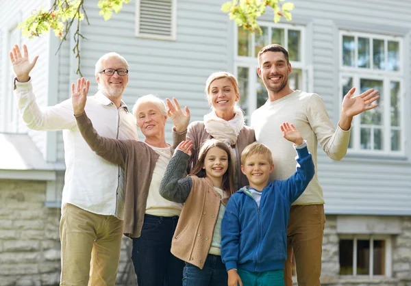 Happy family waving hands in front of house — Stock Photo, Image