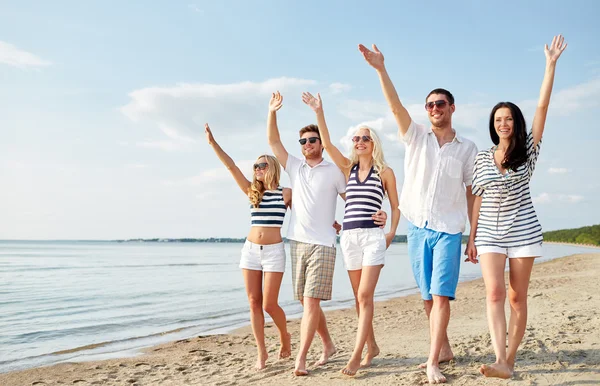 Glimlachend vrienden lopen op strand en zwaaien handen — Stockfoto