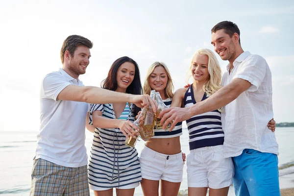 Amici sorridenti clinking bottiglie sulla spiaggia — Foto Stock