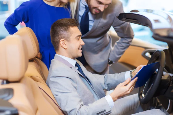 Casal feliz com revendedor de carro em auto show ou salão — Fotografia de Stock