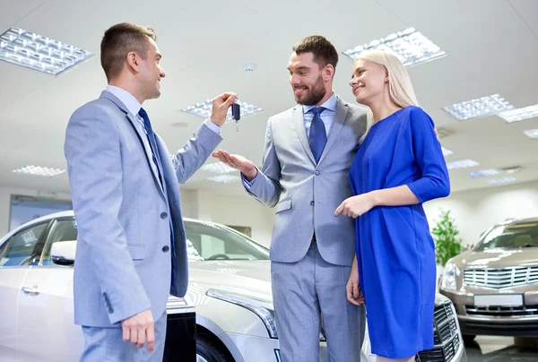 Casal feliz com revendedor de carro em auto show ou salão — Fotografia de Stock
