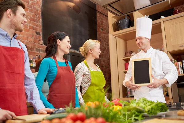 Счастливые друзья и шеф-повар с меню на кухне — стоковое фото