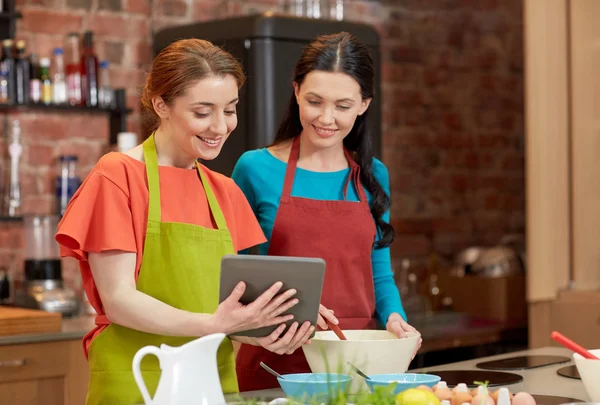 Mulheres felizes com tablet pc cozinhar na cozinha — Fotografia de Stock