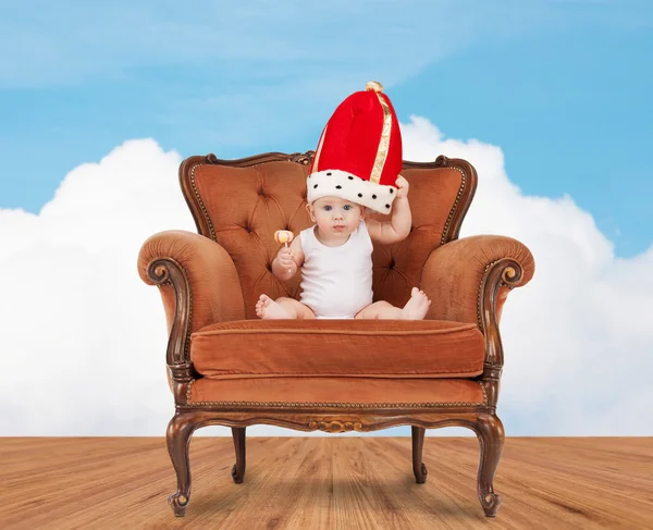 Dítě v royal klobouk s lízátko, sedí na židli — Stock fotografie