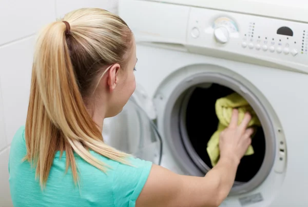 Mujer feliz poniendo la ropa en la lavadora en casa —  Fotos de Stock