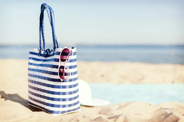 Strohhut, Sonnenbrille und Tasche liegen im Sand — Stockfoto