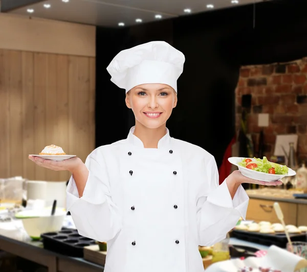 Lachende vrouwelijke chef-kok met salade en taart op platen — Stockfoto