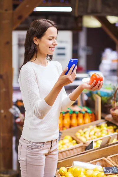 Glad kvinna med smartphone och tomat i marknaden — Stockfoto