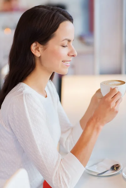 Smiling young woman drinking coffee at cafe — Stock Photo, Image
