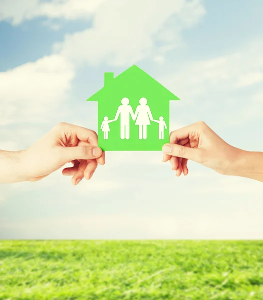 Mãos segurando casa verde com a família — Fotografia de Stock
